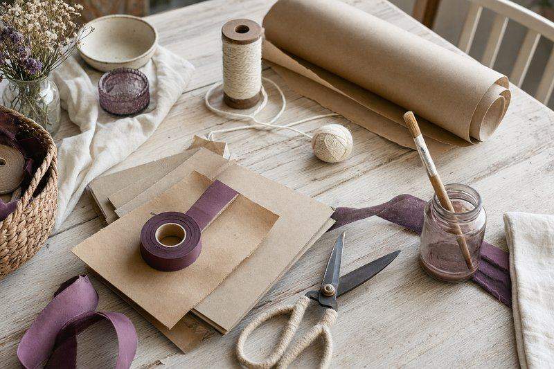 A flatlay of DIY craft supplies including cardboard, scissors, kraft paper, and twine on a table — AI-generated image