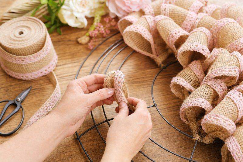Burlap ribbon loops being tied onto a wire wreath form, partway around the ring — AI-generated image
