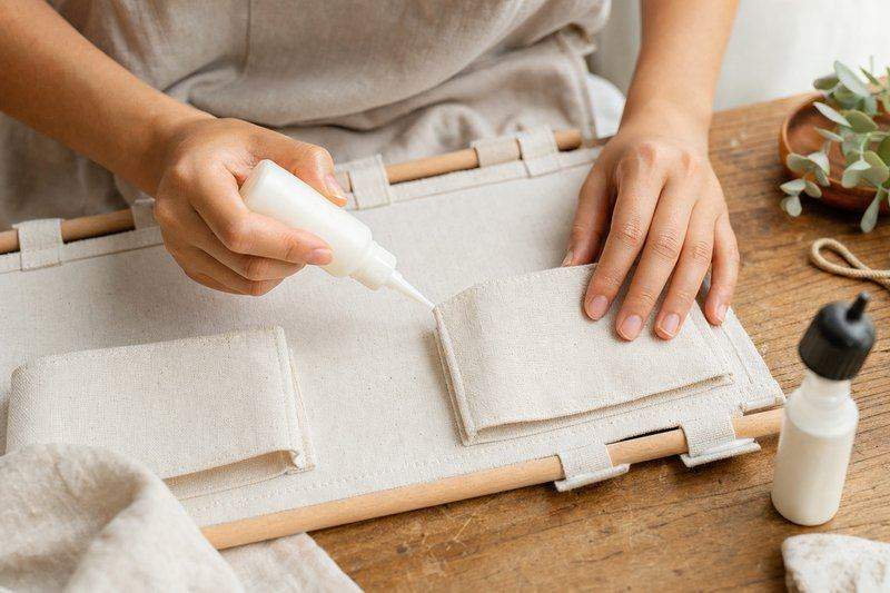 Hands using fabric glue to attach a canvas pocket onto a hanging wall organizer, mid-assembly — AI-generated image