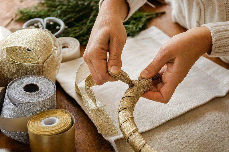 Hands wrapping a wire wreath form with metallic gold ribbon to build a New Year's wreath base — AI-generated image