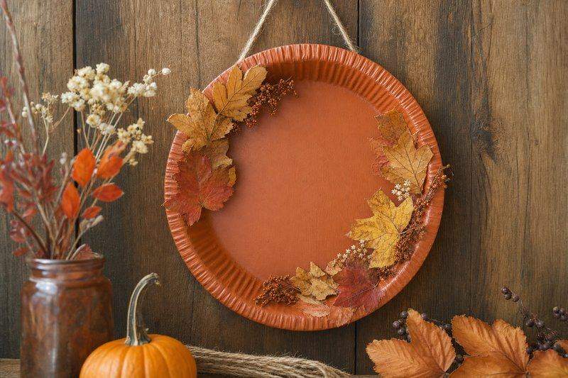 An old pie tin painted rust-orange and turned into a fall-themed wall decoration with dried leaves — AI-generated image