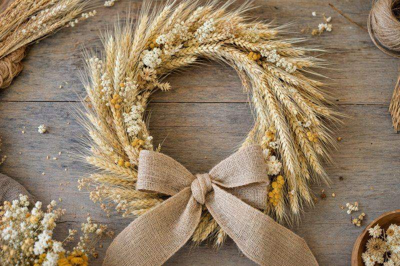 A finished wheat wreath with a burlap ribbon bow and small dried flowers tucked among the stalks — AI-generated image