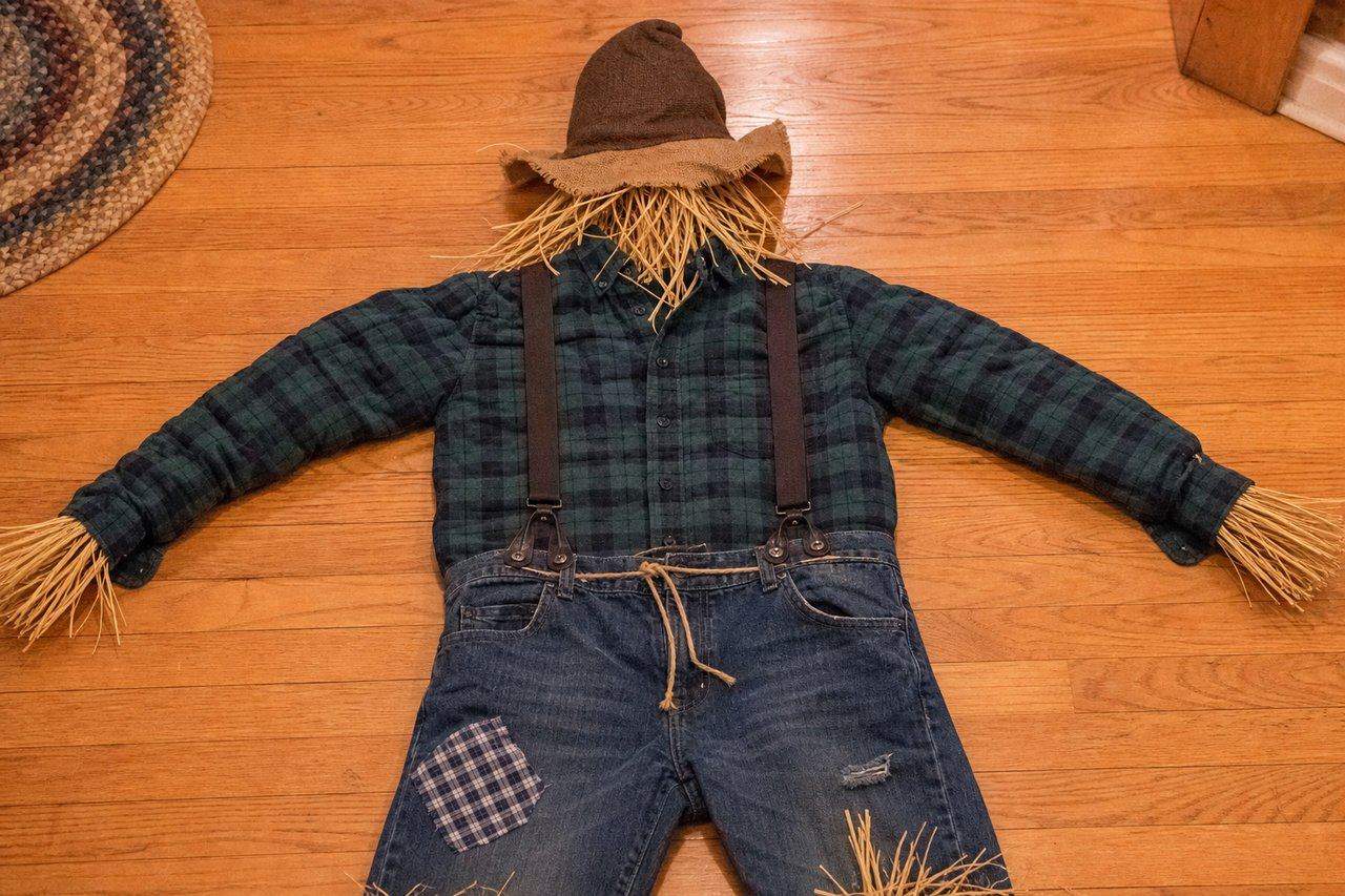 A homemade scarecrow costume made from an old flannel shirt, suspenders, and straw, laid out ready — AI-generated image
