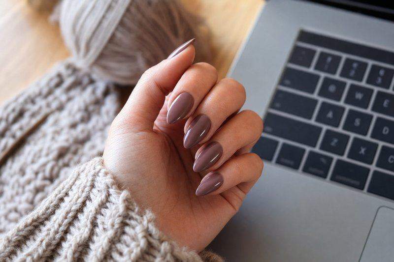 A hand with muted mauve almond-shaped nails resting near a laptop — AI-generated image