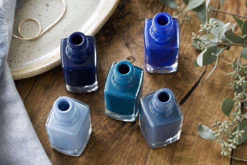 Five open nail polish bottles in a range of blue shades arranged on a wooden table — AI-generated image