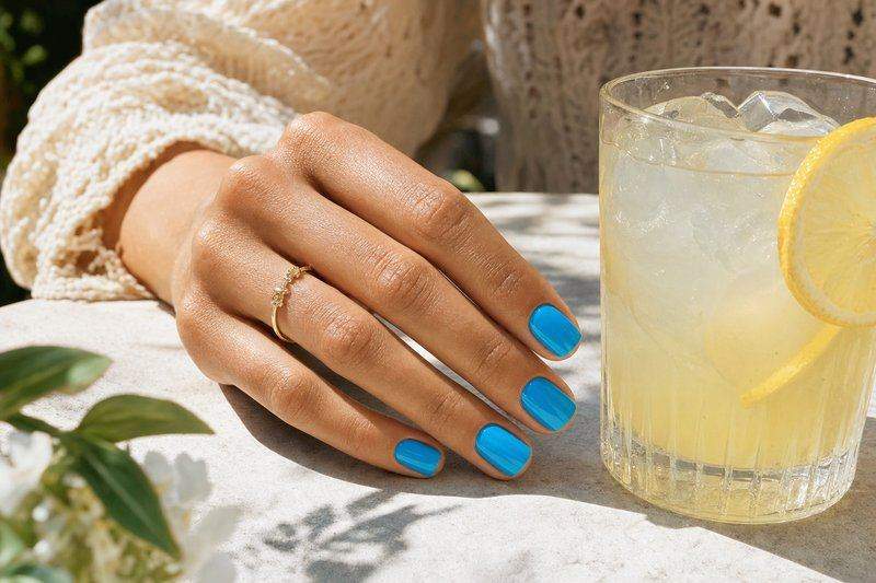 A hand with bright turquoise sky-blue nails near a glass of iced lemonade — AI-generated image