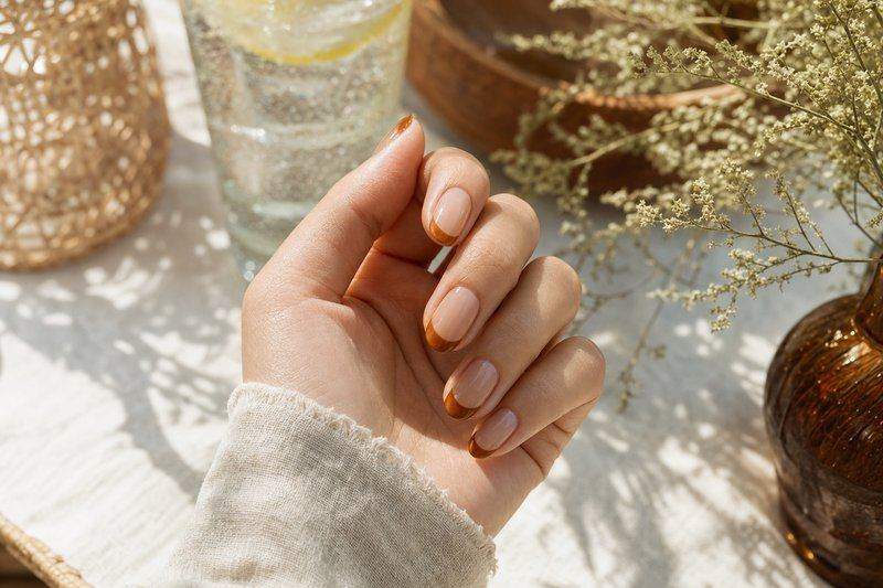 A hand with a warm caramel French tip over a sheer nude base — AI-generated image