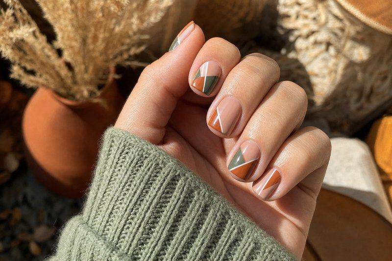 A hand with geometric nail art in a modern terracotta and sage green color pairing — AI-generated image