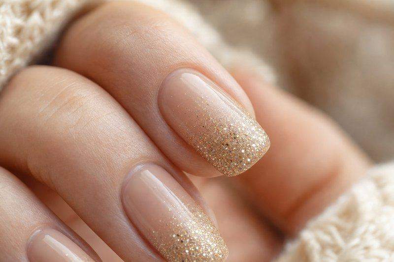 Fingertips with a glitter gradient fading from sheer nude to fine gold glitter at the tip — AI-generated image