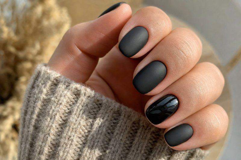 A hand with matte black polish on most nails and one glossy accent nail in the same color — AI-generated image