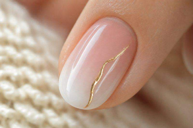 Close-up of one fingernail with a soft pink-to-white gradient base and a delicate gold line accent — AI-generated image